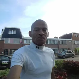 Man in wit shirt poseert voor de camera buiten een woonwijk