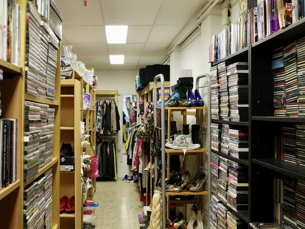 Winkelinterieur met gele en zwarte rekken vol cd's, dvd's en kleding langs beide zijden van een gang