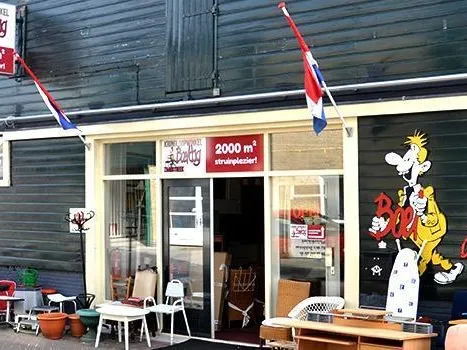 Voorgevel van kringloopwinkel met houten afwerking, grote ramen, Nederlandse vlag en decoraties in etalage