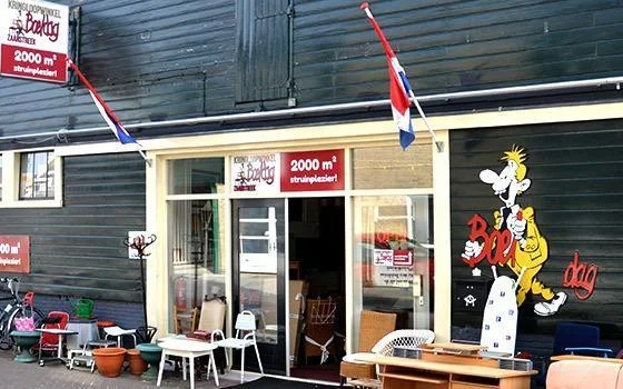 Voorgevel van kringloopwinkel met houten afwerking, grote ramen, Nederlandse vlag en decoraties in etalage