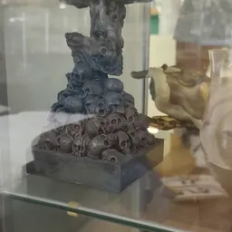 Gesneden stenen sculptuur met gestapelde gezichten en decoratieve elementen op zwart sokkel