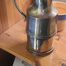Vintage metalen melkkan met twee compartimenten en zwart handvat op houten tafel