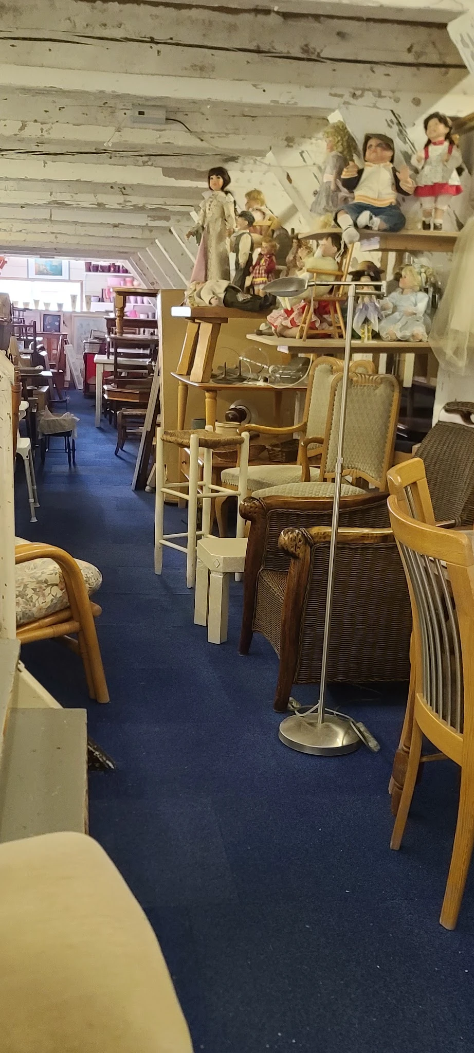 Interieur van kringloopwinkel met diverse meubels: houten stoelen, eetkamerstoelen en tafels netjes uitgestald op blauwe vloe
