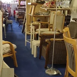 Interieur van kringloopwinkel met diverse meubels: houten stoelen, eetkamerstoelen en tafels netjes uitgestald op blauwe vloe