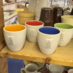 Vier witte koffiekopjes met gekleurde binnenkant (oranje, rood, blauw, groen) en huisje-motief