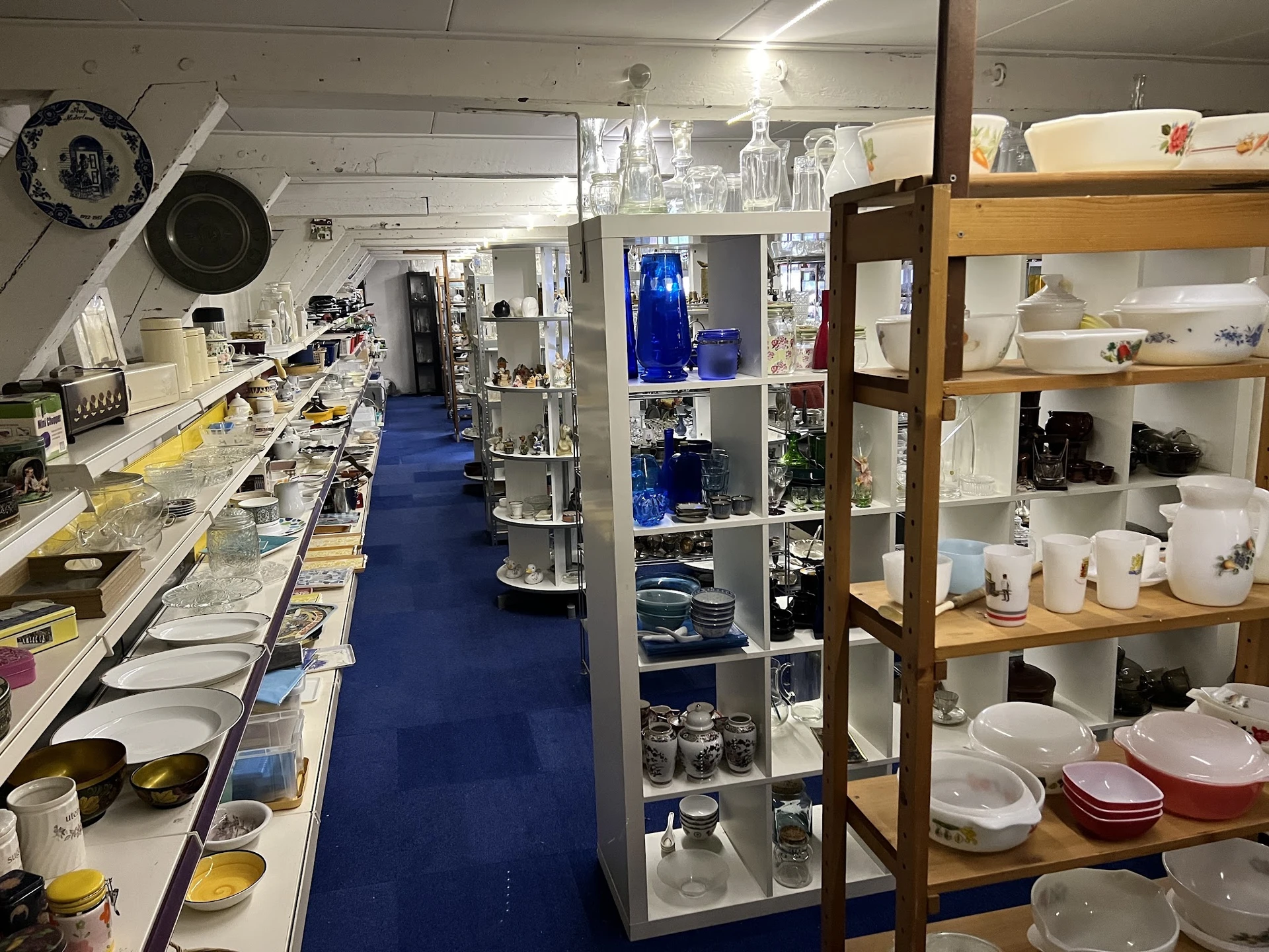 Winkelvloer van kringloopwinkel met stellingen en uitgestalde serviesgoed, glazen en keukengerei