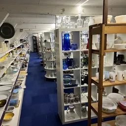 Winkelvloer van kringloopwinkel met stellingen en uitgestalde serviesgoed, glazen en keukengerei