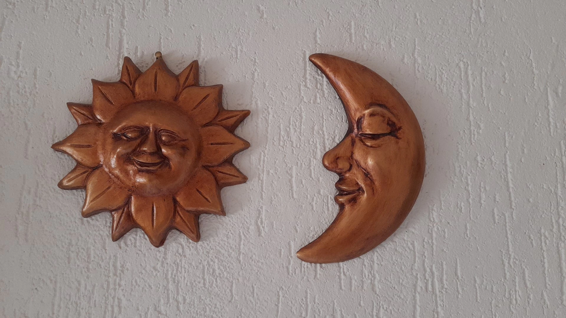 Twee houten decoratieve wandstukken: een lachende zon en een grijnzende maan