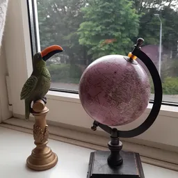 Decoratief vogelfiguur met rood en groen gevederte naast een paarse wereldbol op een vensterbank
