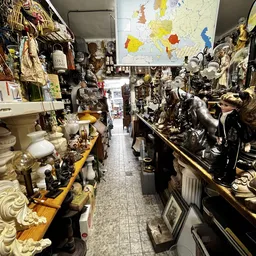 Lange winkelgang vol met beeldhouwwerken, figuren en decoratieve objecten op planken en displays aan beide zijden