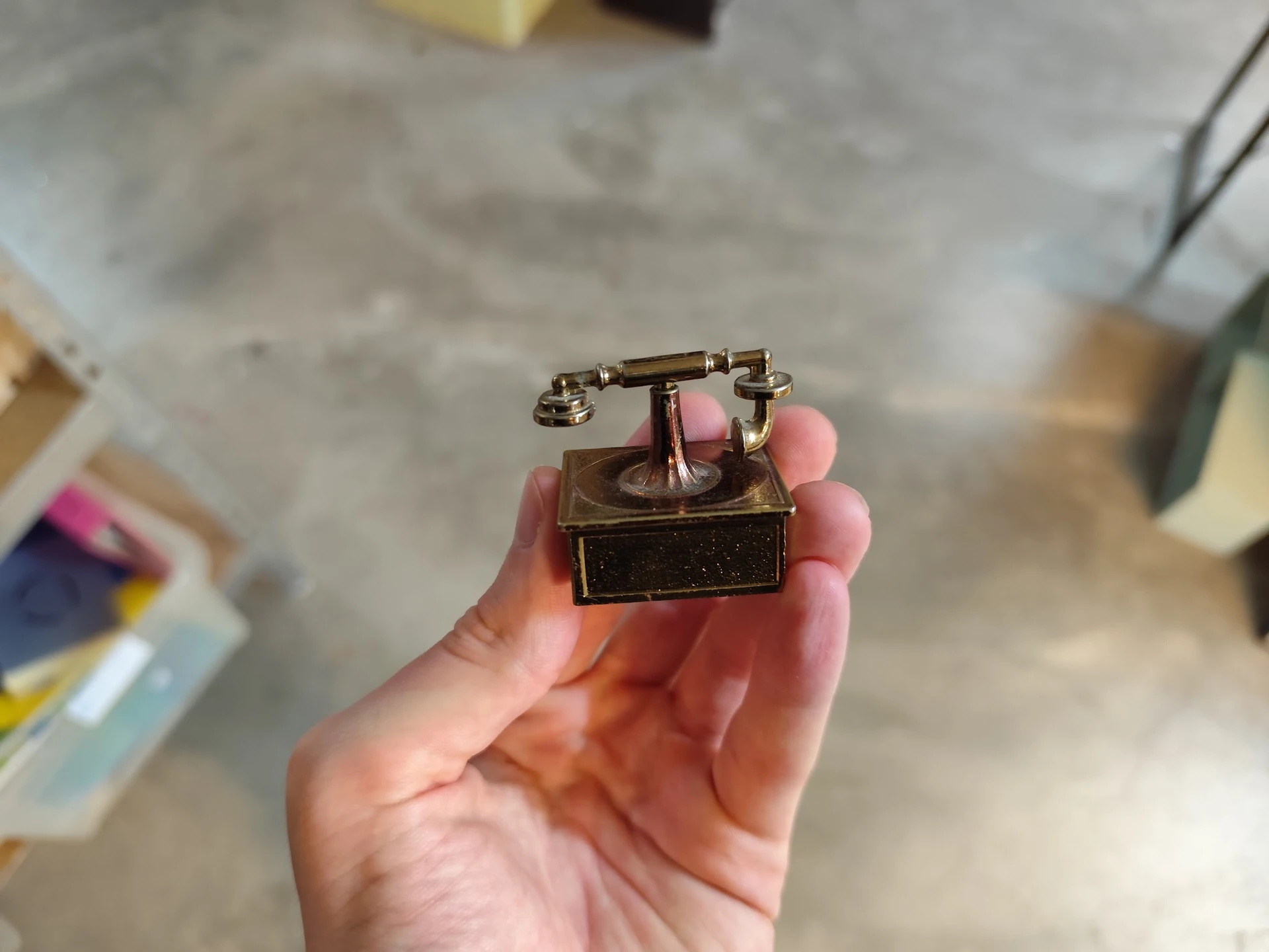Vintage telefoon met draaischijf in bronskleurig metaal, gehouden in een hand