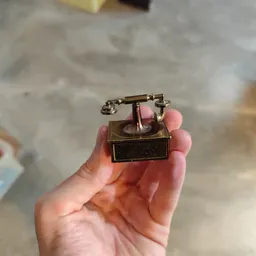 Vintage telefoon met draaischijf in bronskleurig metaal, gehouden in een hand