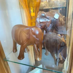 Drie houten beeldhouwwerken van olifanten in verschillende bruine tinten in een vitrine