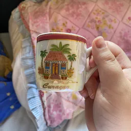 Close-up van een vintage mok met decoratie van een palmboom en huisje, gehouden in een hand