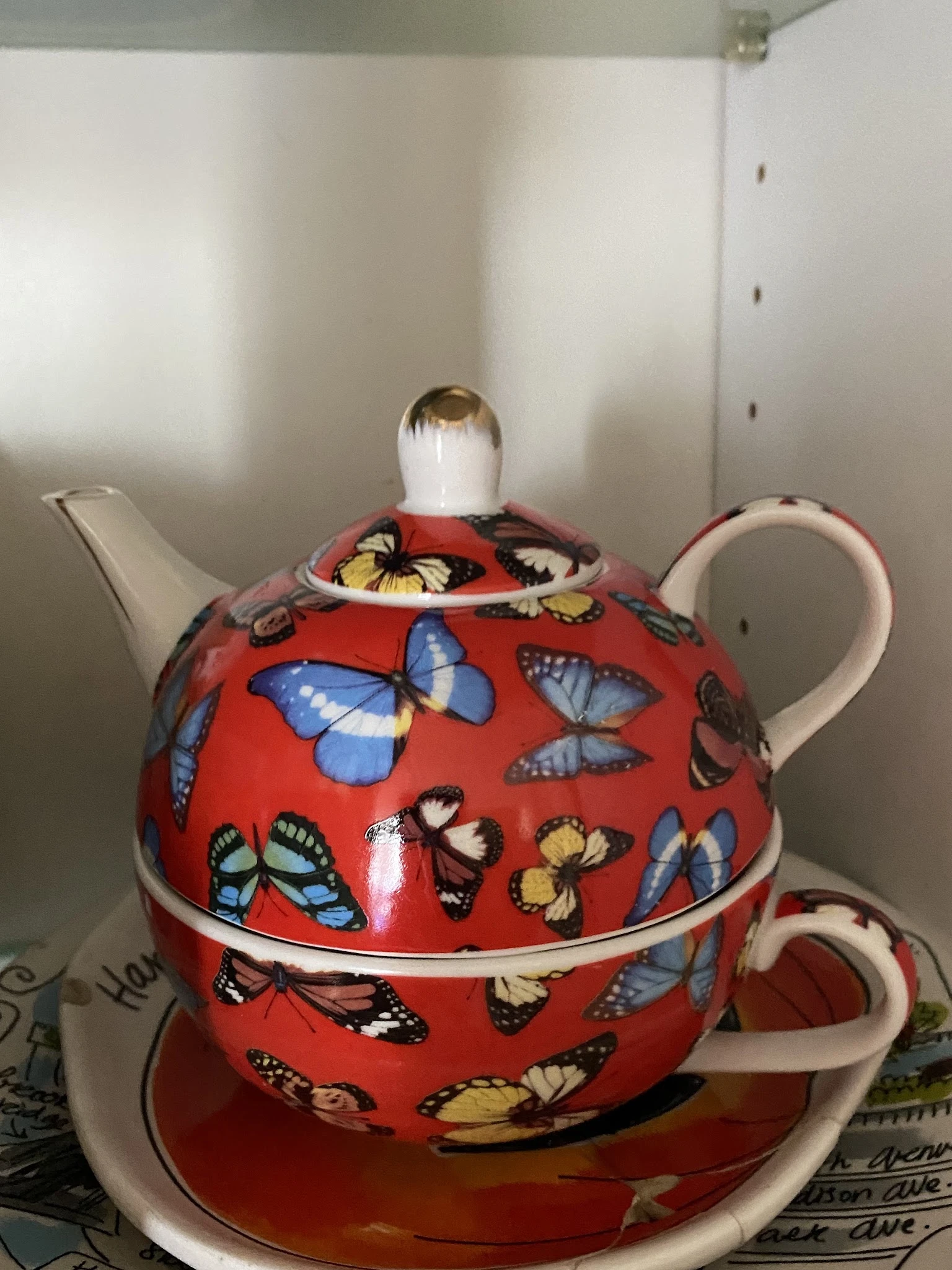 Rode porseleinen theepot met vlinders en bloemen in verschillende kleuren