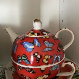 Rode porseleinen theepot met vlinders en bloemen in verschillende kleuren