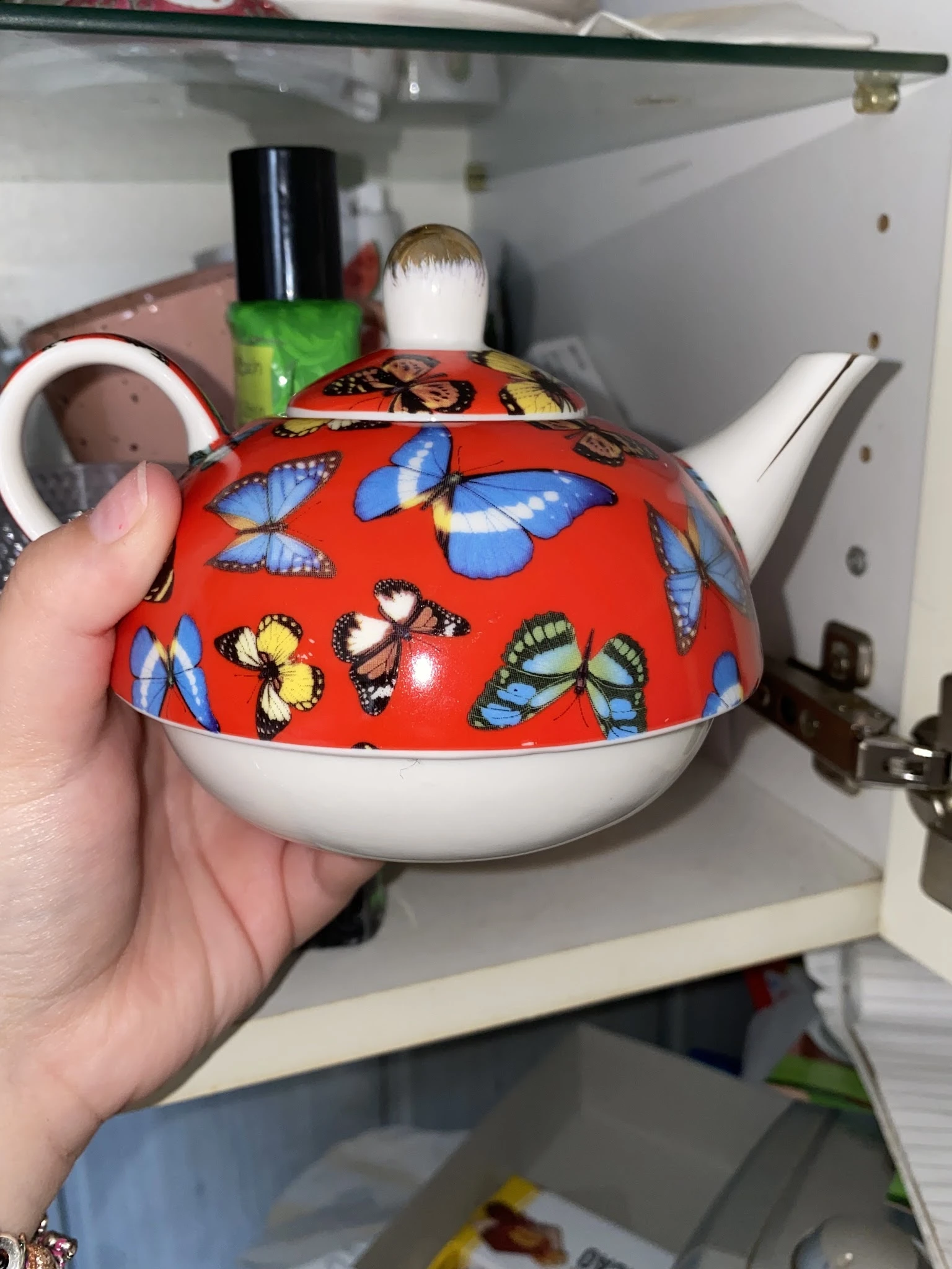 Rode theepot met kleurrijke vlinderdecoratie, wit onderwerk, gehouden in hand