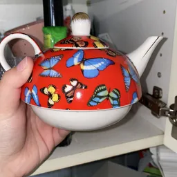 Rode theepot met kleurrijke vlinderdecoratie, wit onderwerk, gehouden in hand
