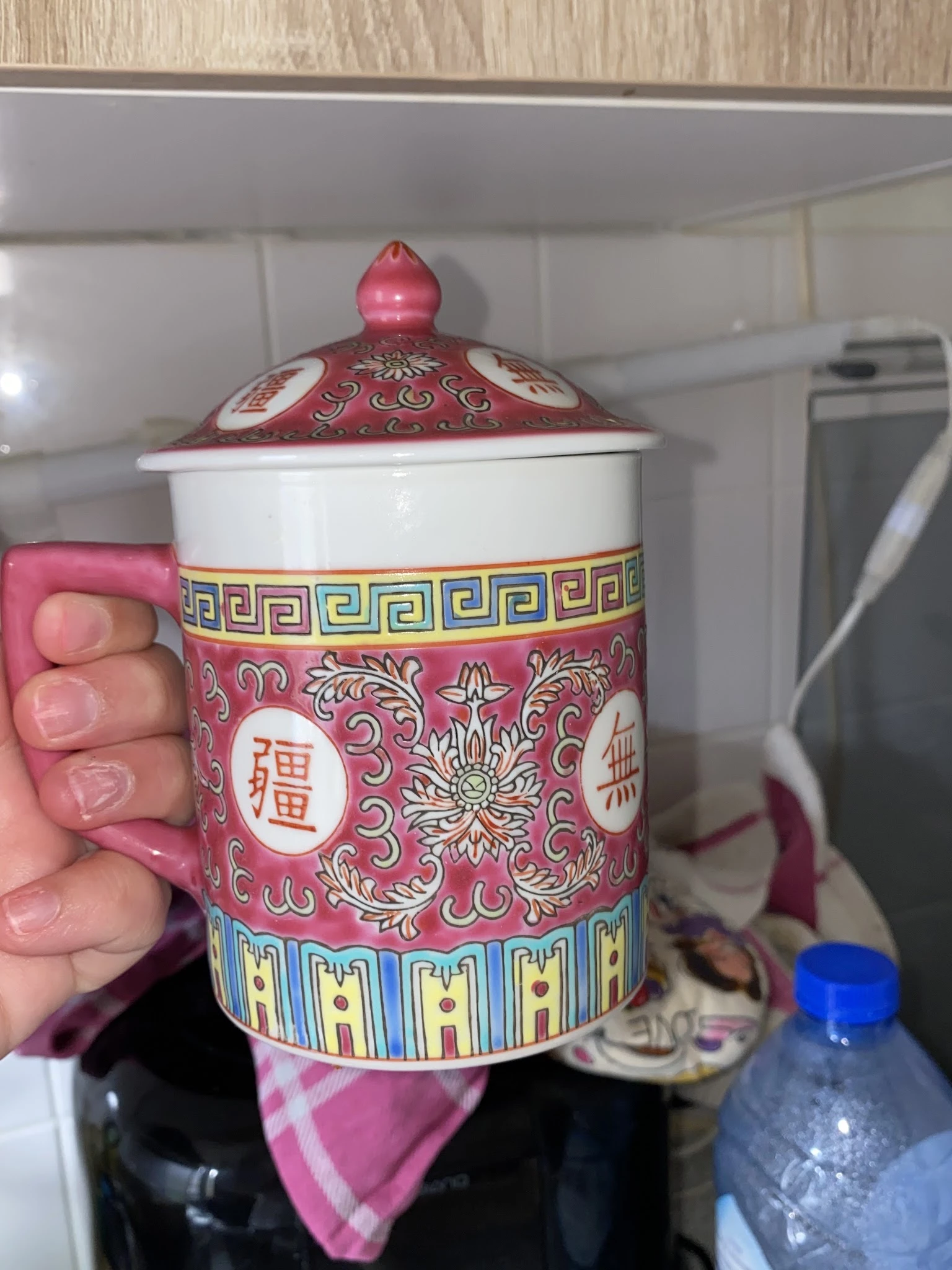 Close-up van een roze porselein dekselkan met Chinees ornament en merktekens, gehouden in hand