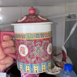Close-up van een roze porselein dekselkan met Chinees ornament en merktekens, gehouden in hand