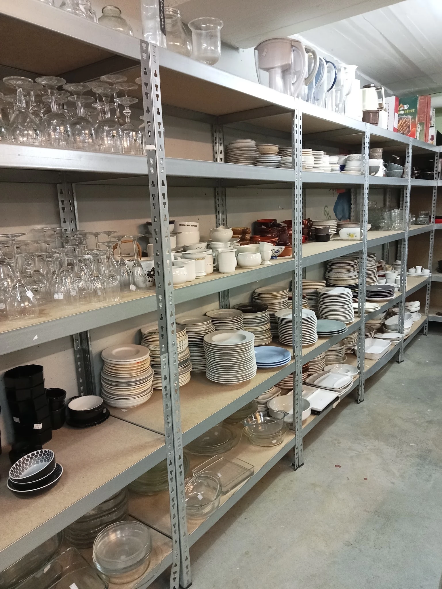 Metalen stellingen met gestapelde borden, servies en glazen in een kringloopwinkel