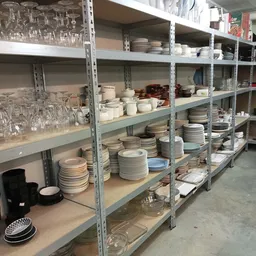 Metalen stellingen met gestapelde borden, servies en glazen in een kringloopwinkel