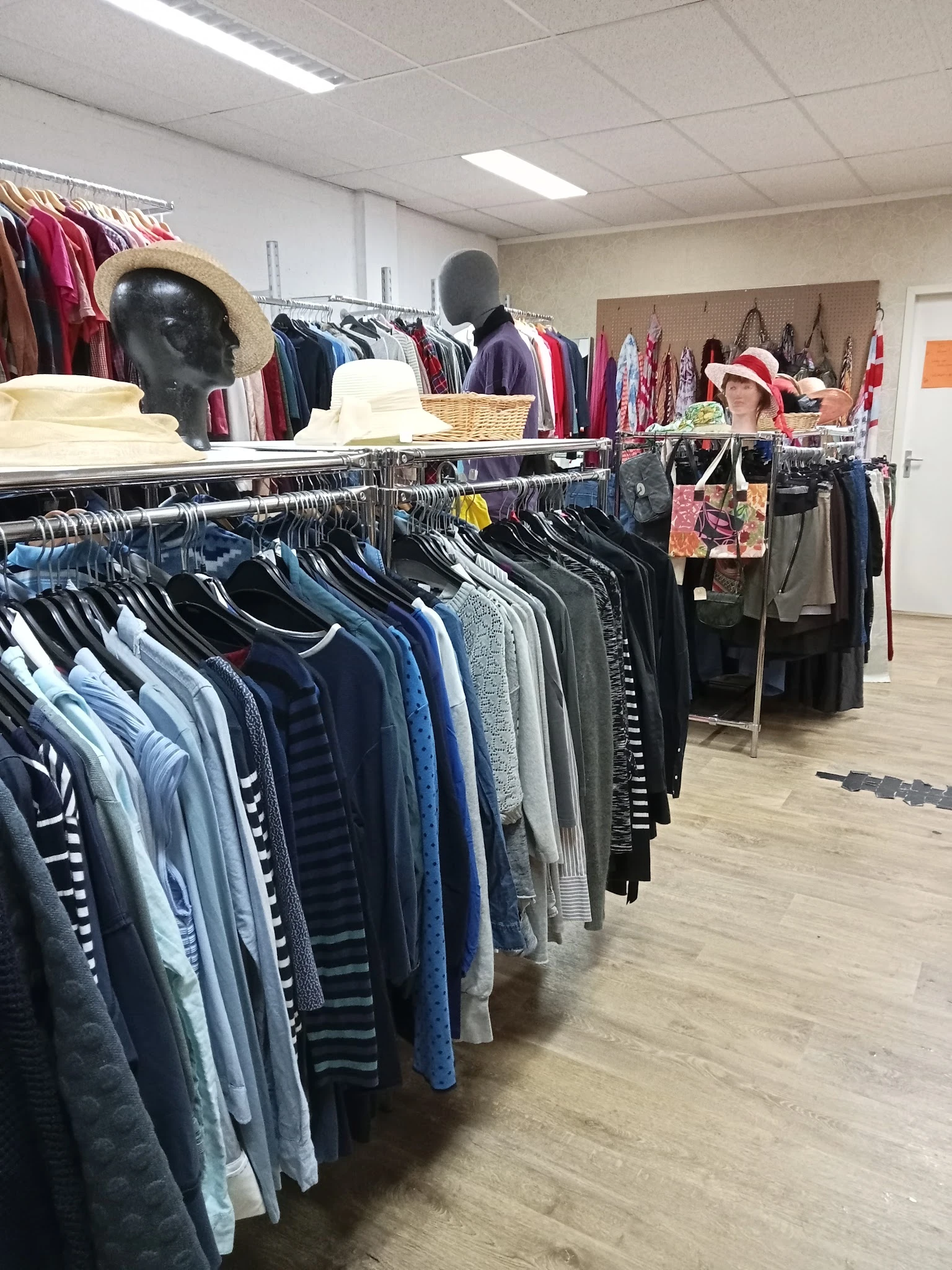 Rekken met tweedehands kleding in verschillende kleuren en maten in de winkel