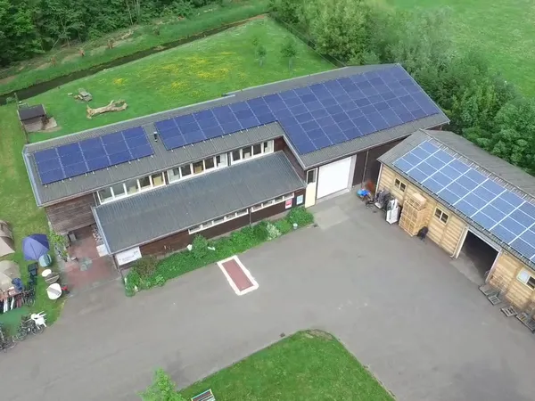 Luchtfoto van kringloopwinkel met zonnepanelen op daken, omgeven door groen