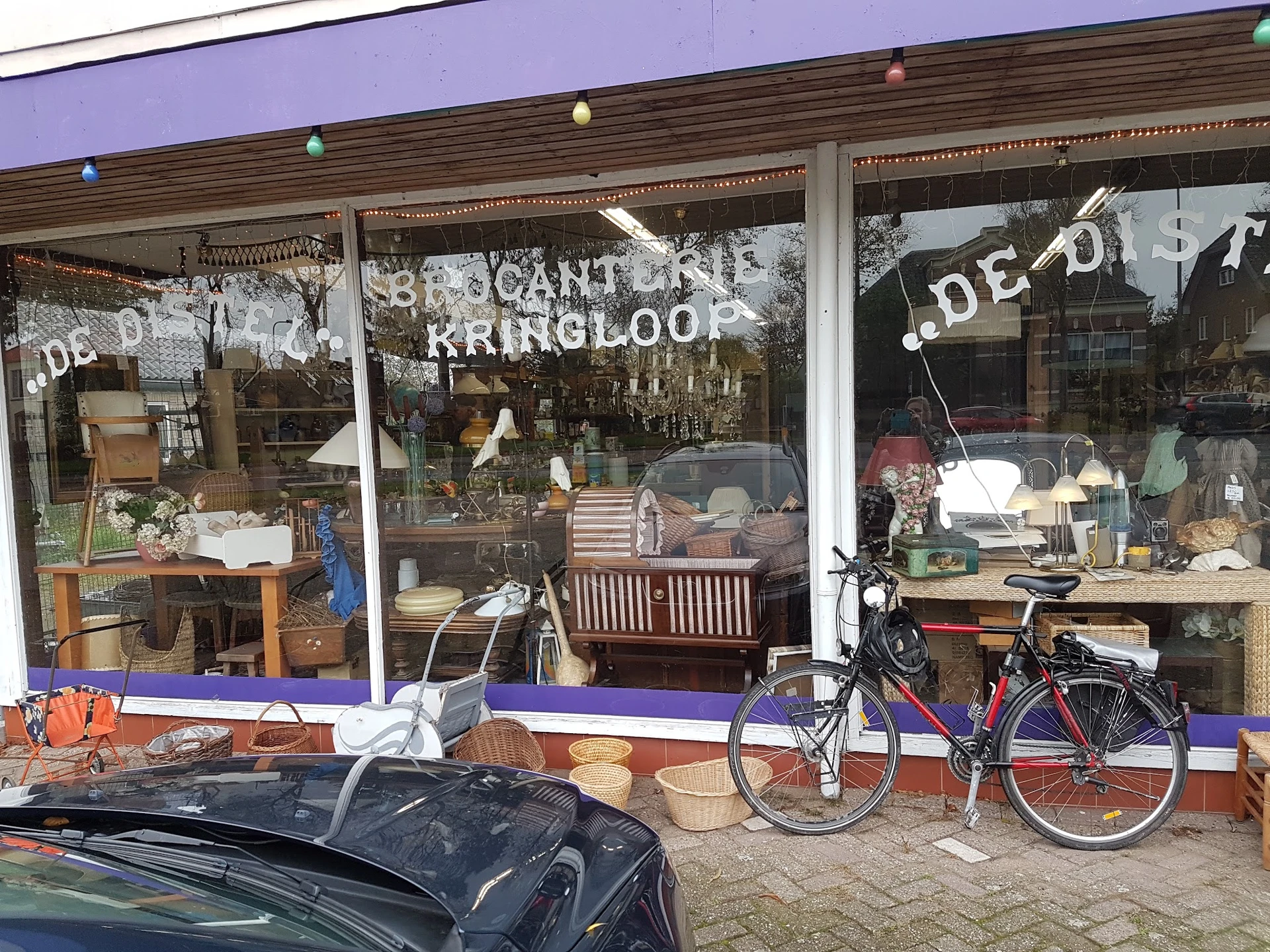 Winkelgevel met vitrines vol meubels, servies en decoratie, fiets vooraan, paarse luifel