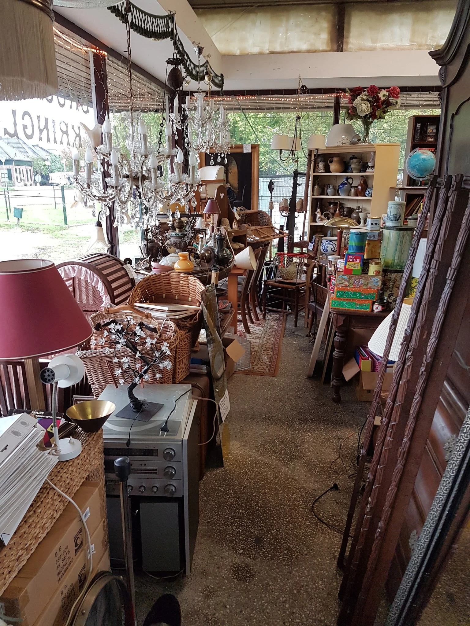 Binnenaanzicht van kringloopwinkel met meubels, lampen, servies en diverse spullen uitgestald