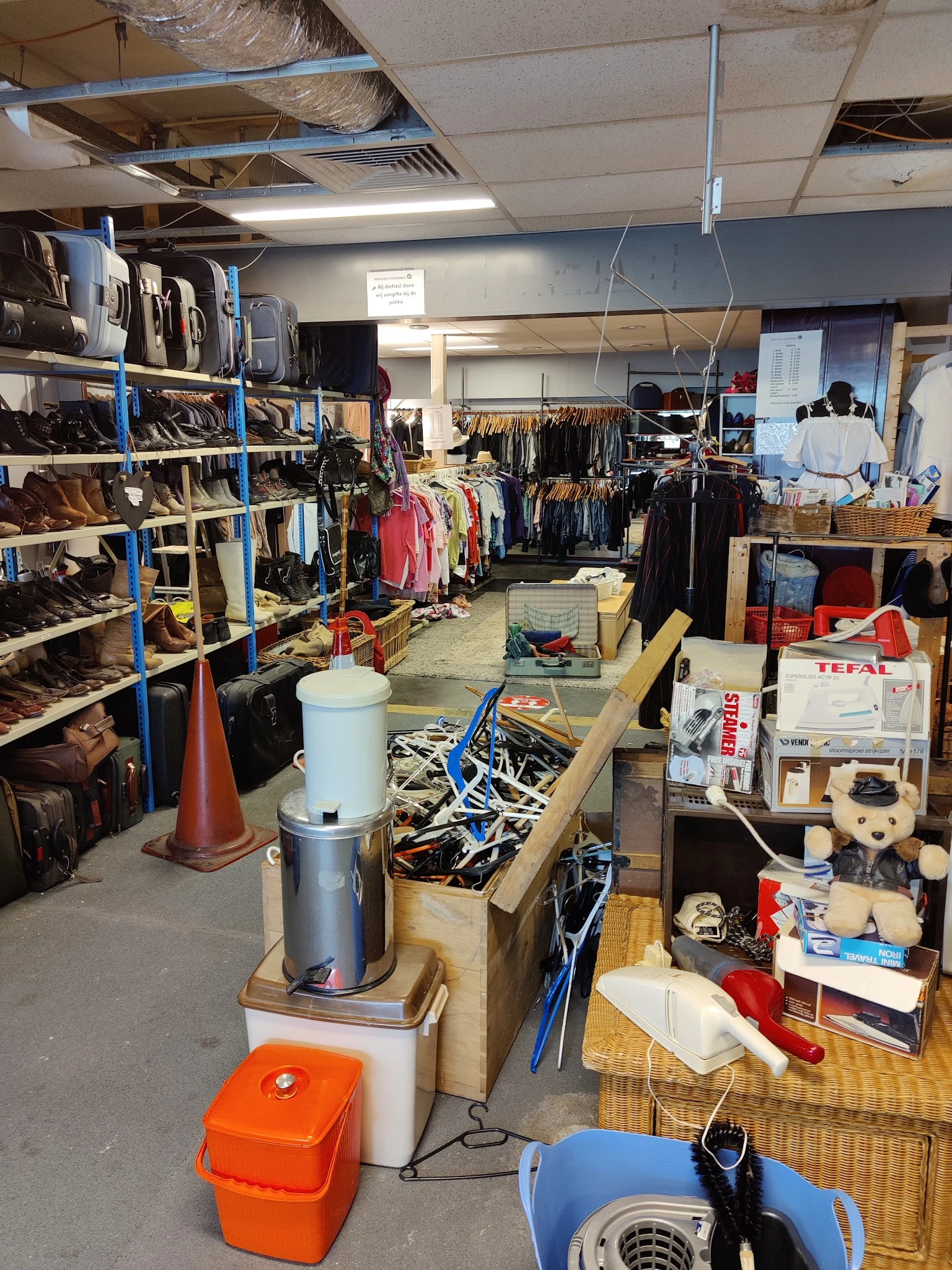 Winkelvloer met stellingen vol schoenen, kleding aan rekken, dozen en huishoudelijke artikelen