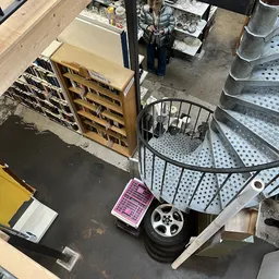 Diverse gebruikte huishoudartikelen en meubels op de winkelvloer, waaronder houten kastje, metalen manden en wielen.