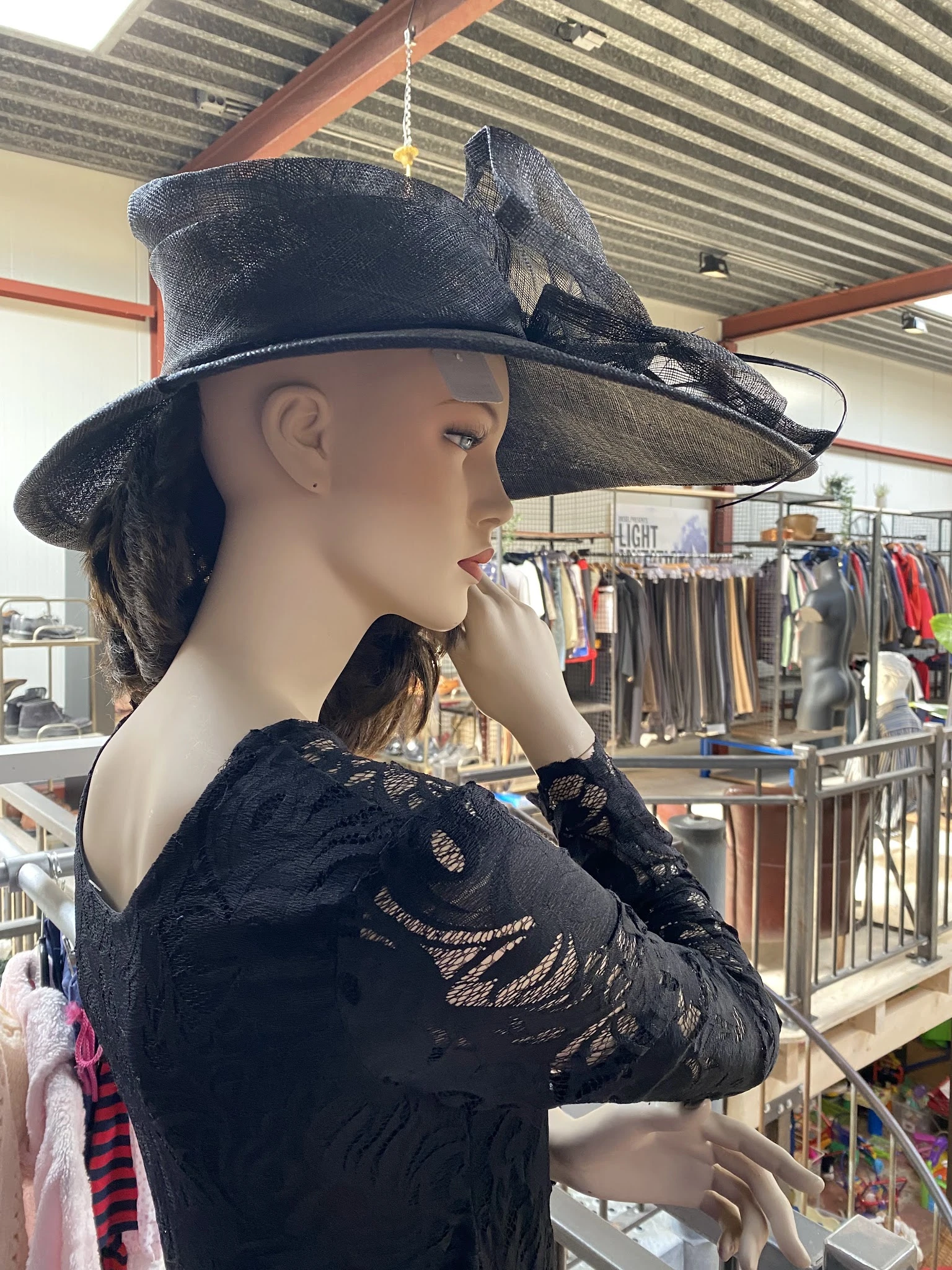 Etalagepop gekleed in zwart kanten kleding en zwarte cowboyhoed, op achtergrond rekken met kleding