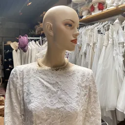 Etalagepop in witte kanten jurk met parelketting, omgeven door rekken met trouwjurken
