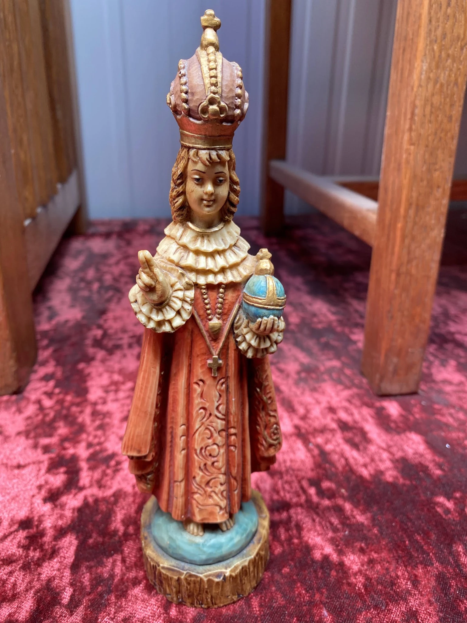 Houten beeldje van een heilige in rood gewaad met gouden details, staand op paars tapijt