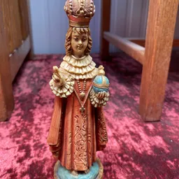 Houten beeldje van een heilige in rood gewaad met gouden details, staand op paars tapijt