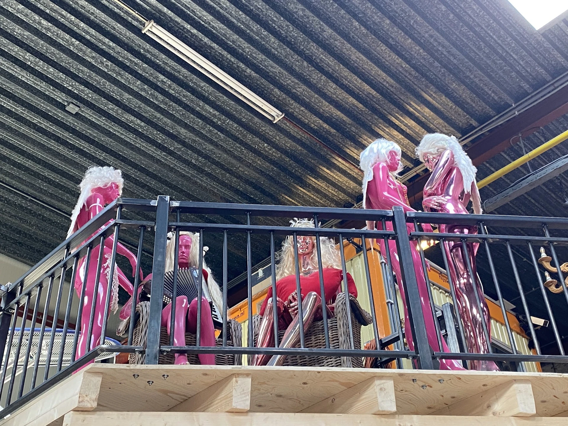 Rekken met roze en rode kleding op een platform onder een golfplaten dak in een kringloopwinkel
