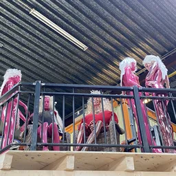 Rekken met roze en rode kleding op een platform onder een golfplaten dak in een kringloopwinkel