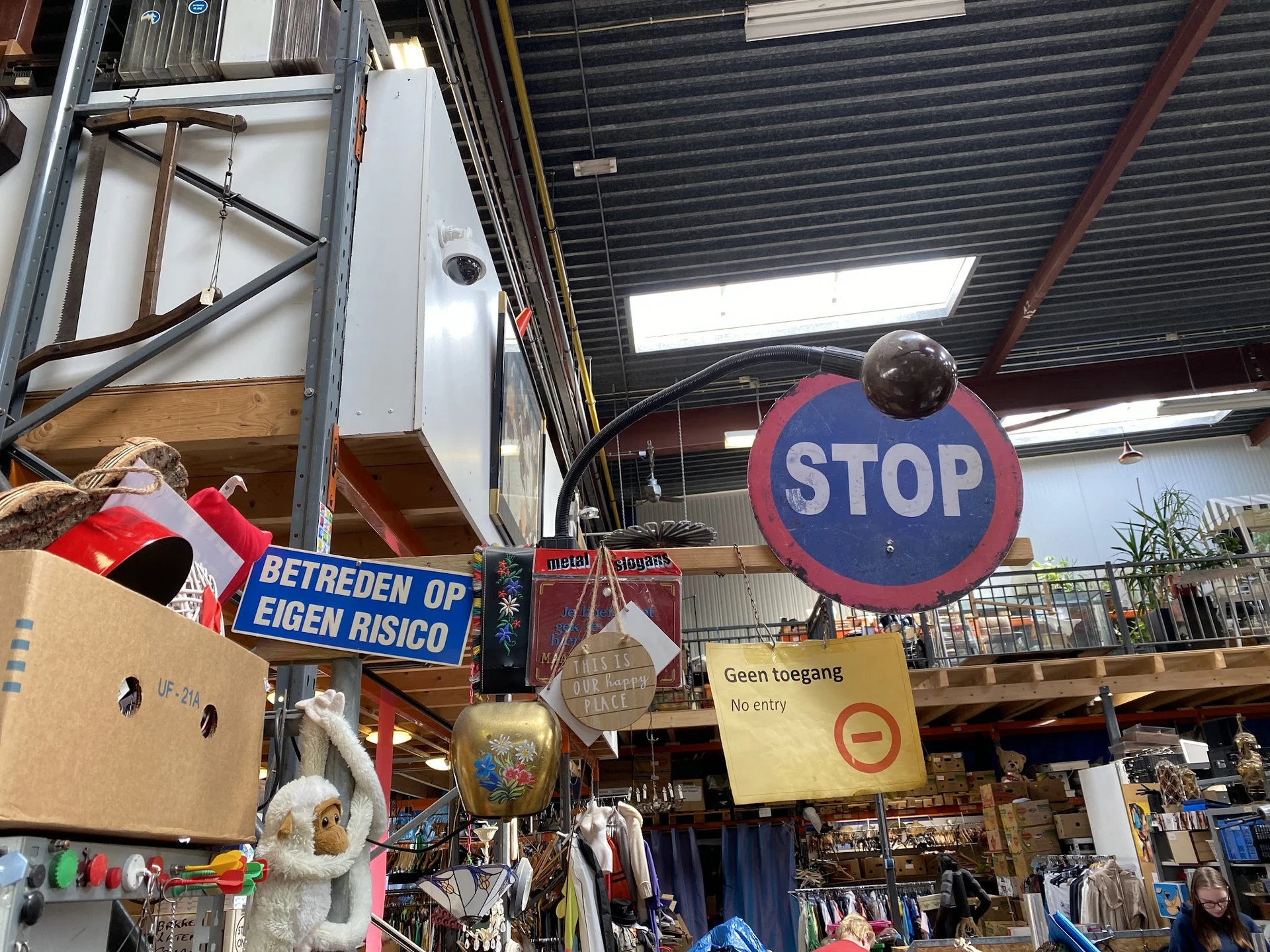 Binnenaanzicht van kringloopwinkel met STOP-bord, vintage spullen en stellingen onder glazen dak