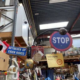 Binnenaanzicht van kringloopwinkel met STOP-bord, vintage spullen en stellingen onder glazen dak