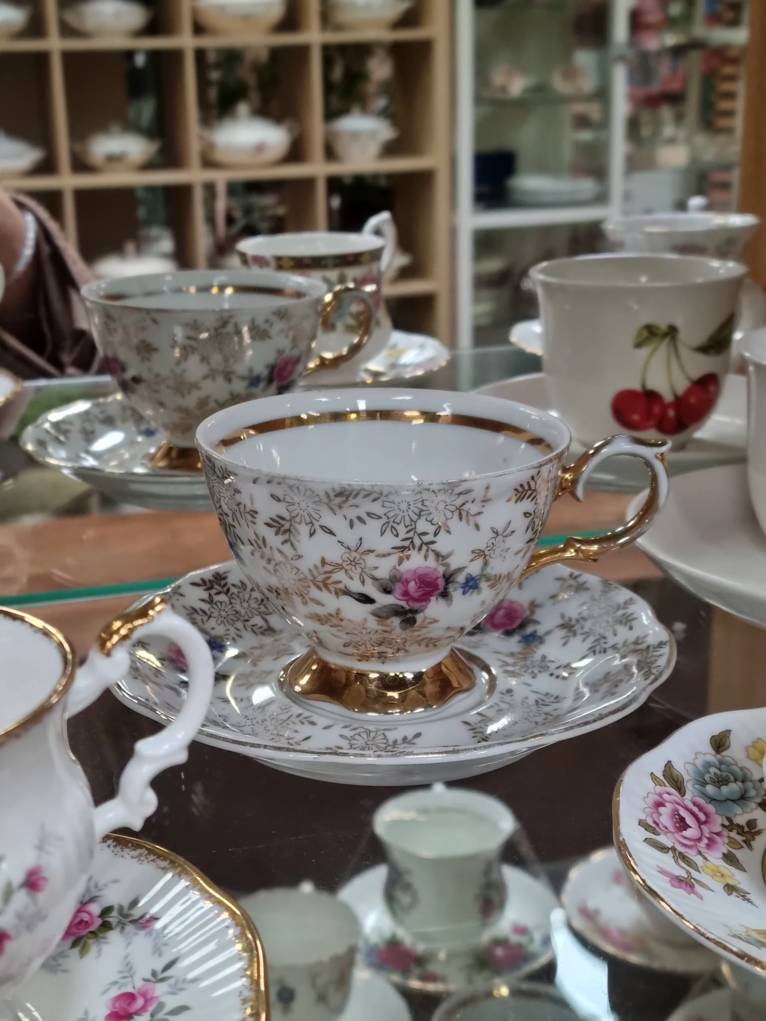 Porseleinen theeservies met bloemenmotief en gouden accenten, voorgrond toont kopje op schotel