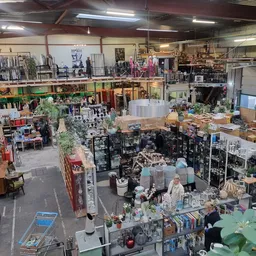 Overzicht van kringloopwinkel met diverse afdelingen, stellingen met spullen, planten en meubilair op meerdere niveaus