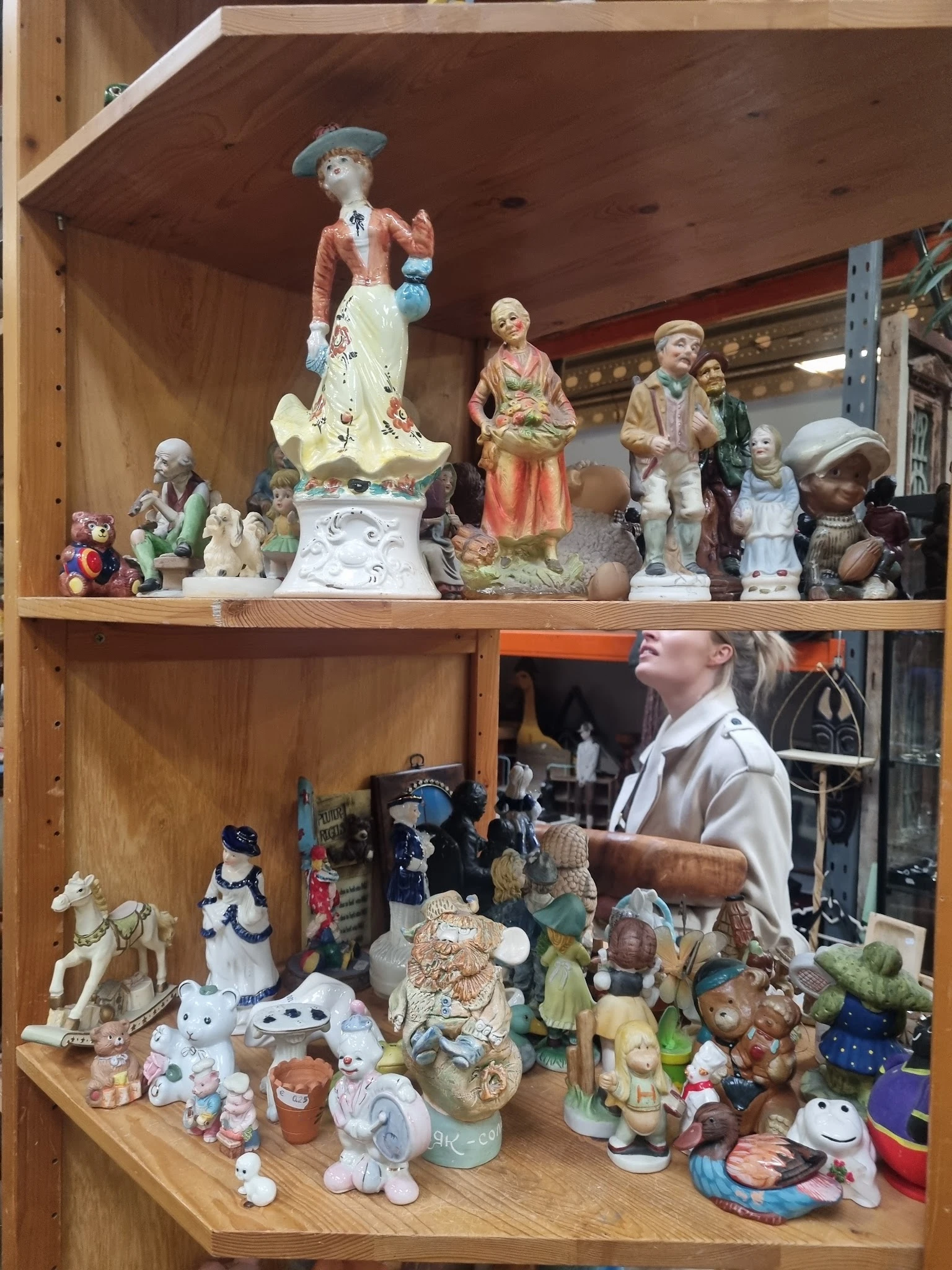 Houten stellingen met diverse decoratieve beeldjes, porseleinfiguren en verzamelobjecten uitgestald