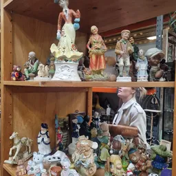 Houten stellingen met diverse decoratieve beeldjes, porseleinfiguren en verzamelobjecten uitgestald