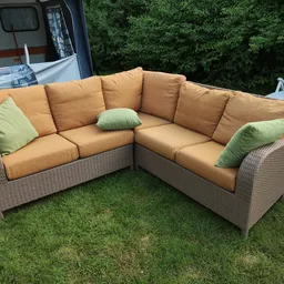 Hoekbank in naturel rattan met gele/goudkleurige kussens en groene sierkussens op grasveld
