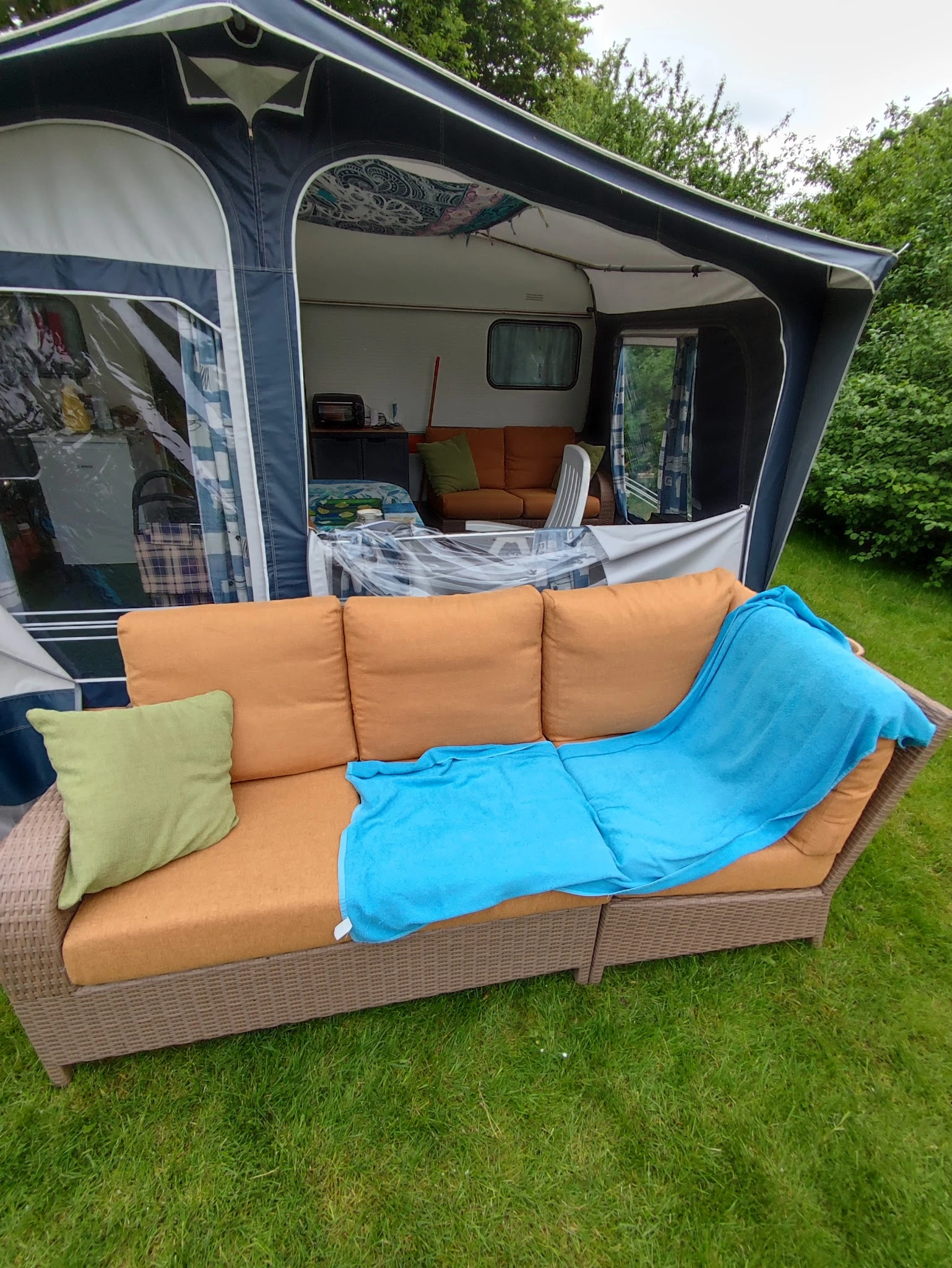 Oranje tuinbank met blauwe deken en gele kussen buiten voor een caravan
