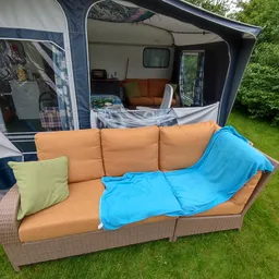 Oranje tuinbank met blauwe deken en gele kussen buiten voor een caravan