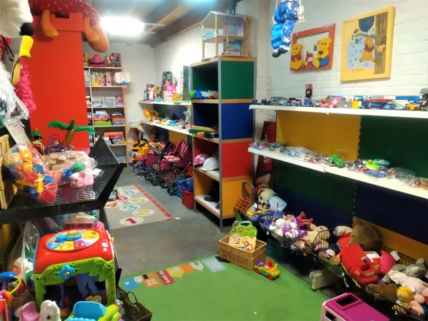 Speelgoedafdeling in kringloopwinkel met gekleurde stellingen, speelgoed, poppen en diverse kinderaccessoires