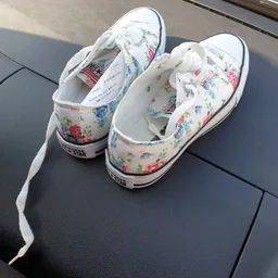 Witte sneakers met bloemenprint en witte veters op grijze ondergrond