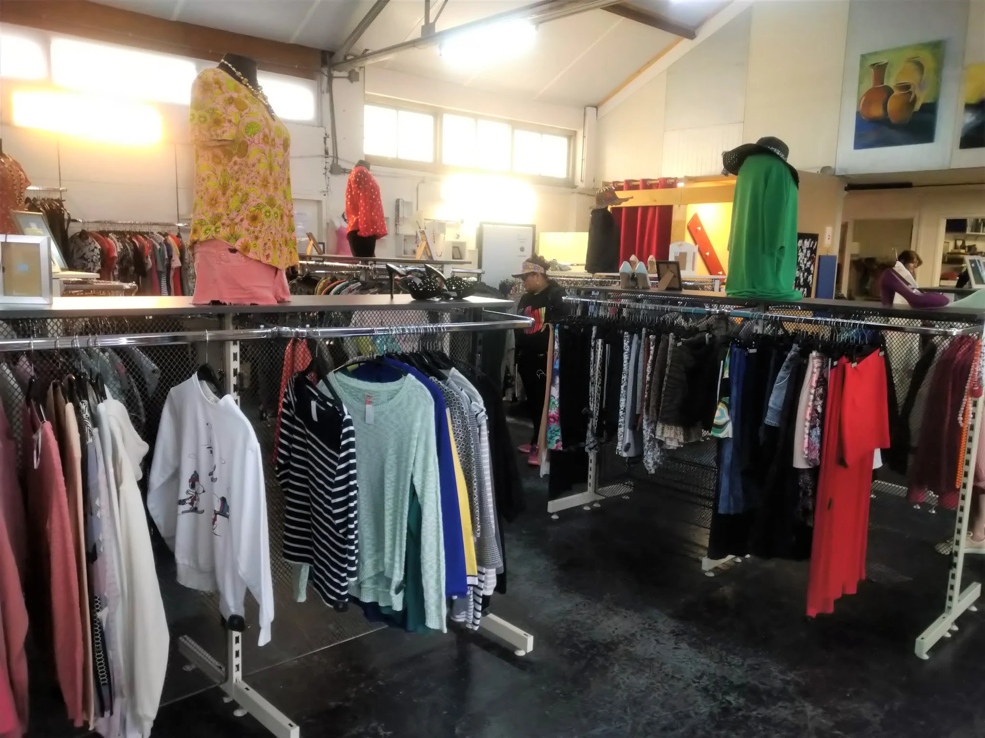 Winkelinterieur met meerdere kledingrekken vol tweedehands kleding, goed verlichte ruimte met hoge plafonds